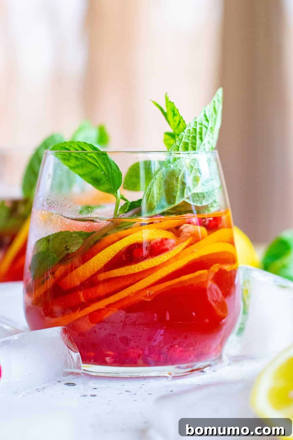 Bright red pomegranate punch garnished with citrus slices, fresh mint, and pomegranate arils. A perfect holiday or brunch drink idea.