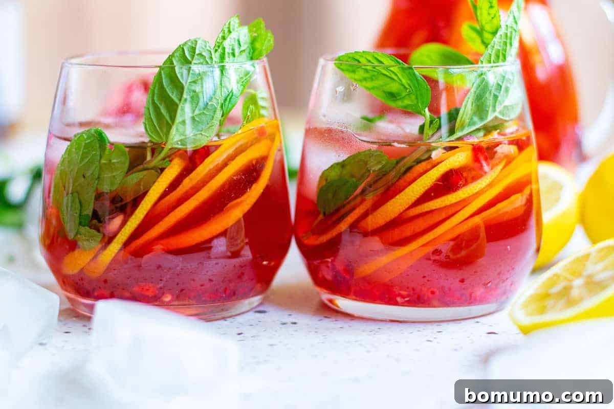 Two elegant stemless glasses filled with bright red sparkling punch, artfully garnished with vibrant citrus slices and fragrant mint leaves, ready to be enjoyed.
