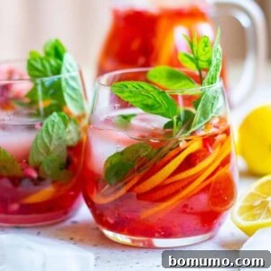 Brightly colored red drink in a stemless glass, full of citrus slices and mint leaves, ready to be enjoyed.