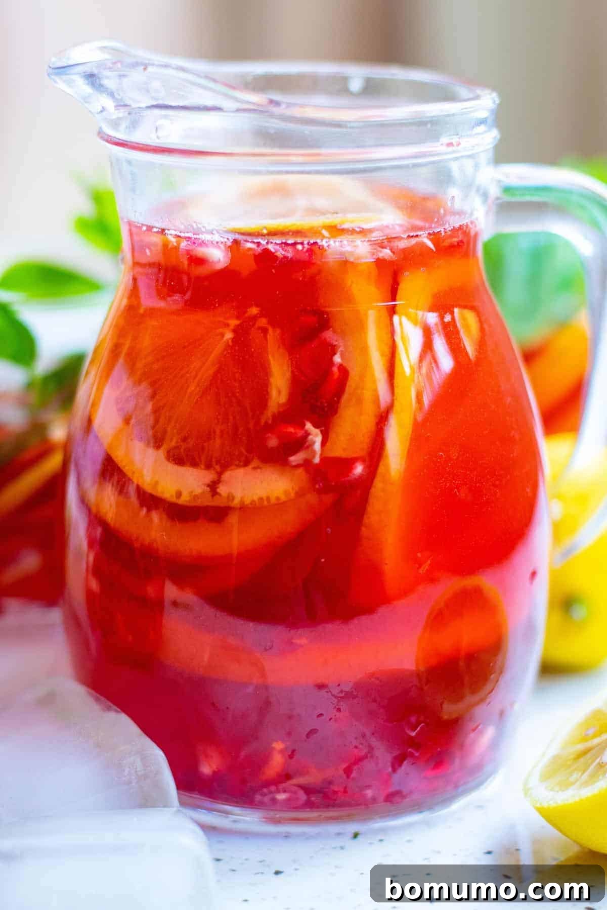 A large pitcher of bright red pomegranate punch, adorned with vibrant citrus slices and ready for serving a refreshing drink.