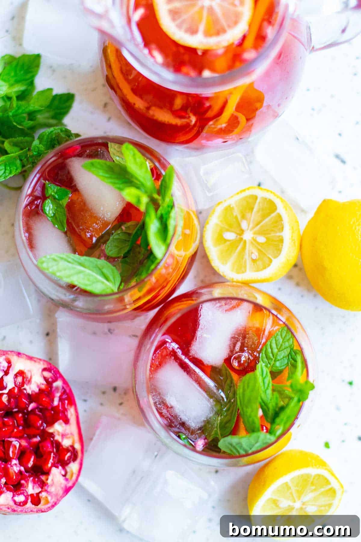 Overhead view of two glasses of sparkling pomegranate punch, elegantly garnished with fresh pomegranate arils and vibrant mint leaves, showcasing its festive appeal.
