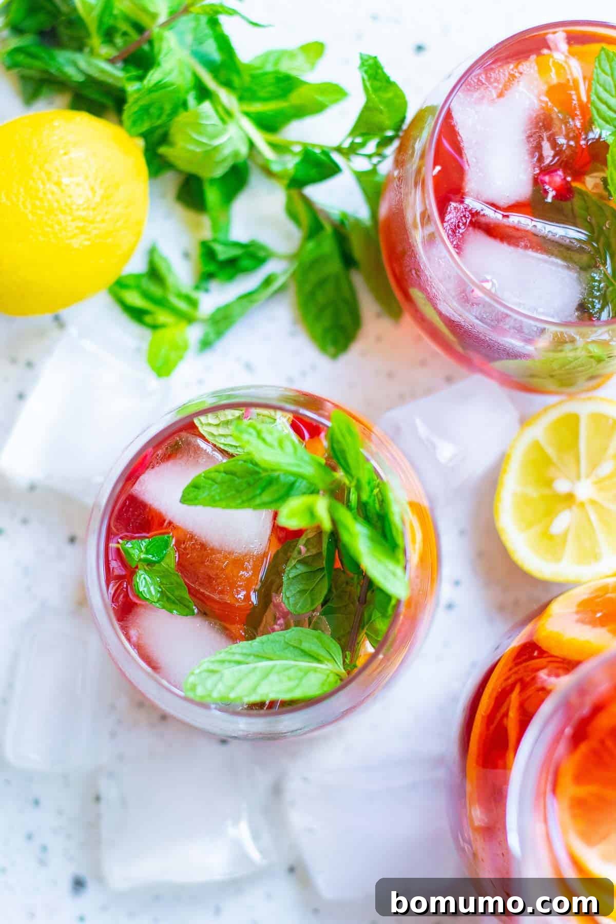 Overhead view of a single glass of bright red sparkling pomegranate punch, garnished with fresh mint leaves and subtle fruit slices.