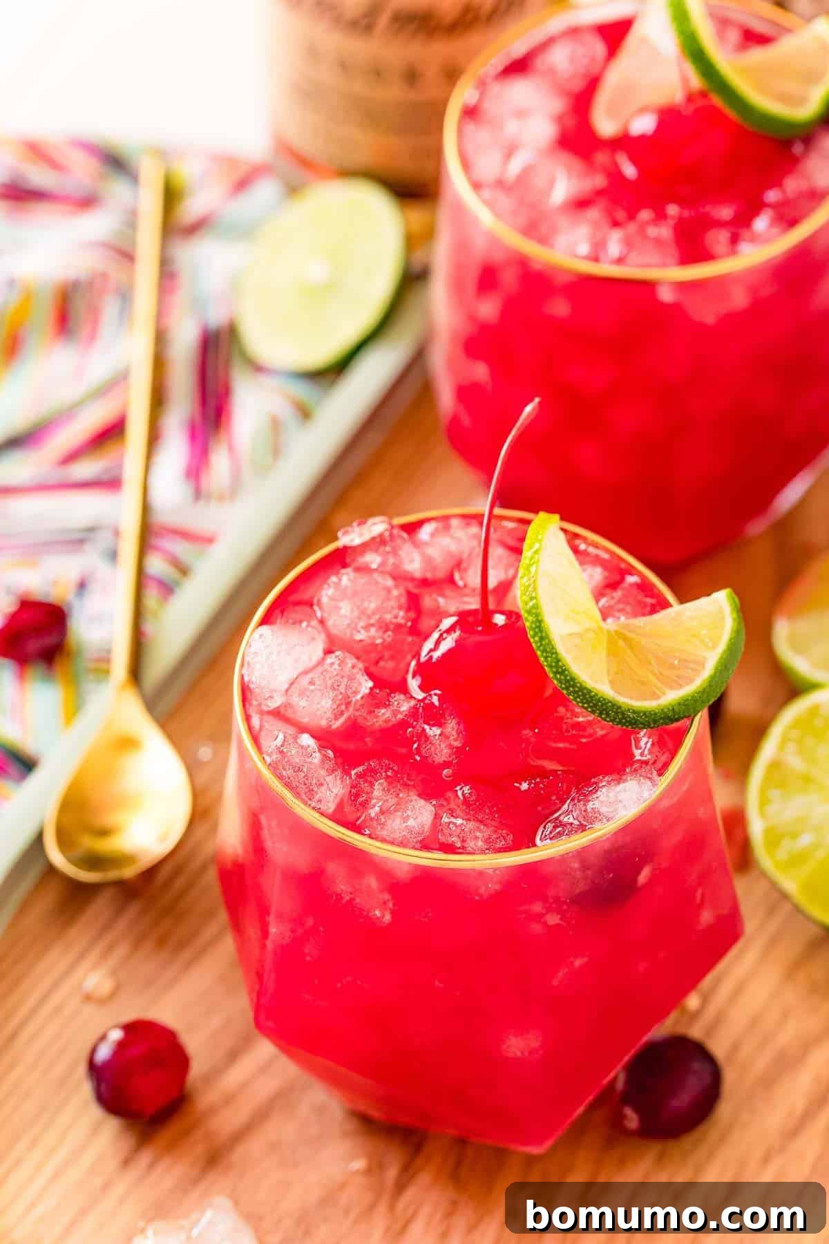 An overhead view of two bright red Bay Breeze drinks, garnished with ice, a cherry, and a lime slice.