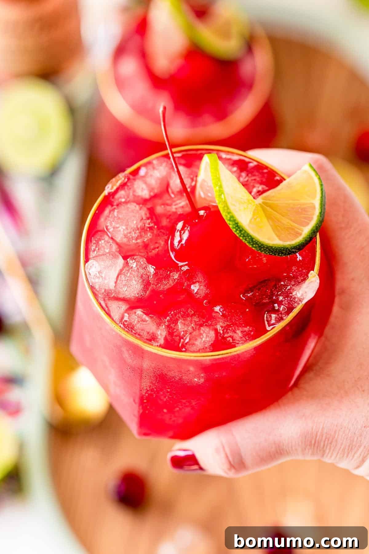 A bright red cocktail held in a person's hand, against a blurred background.