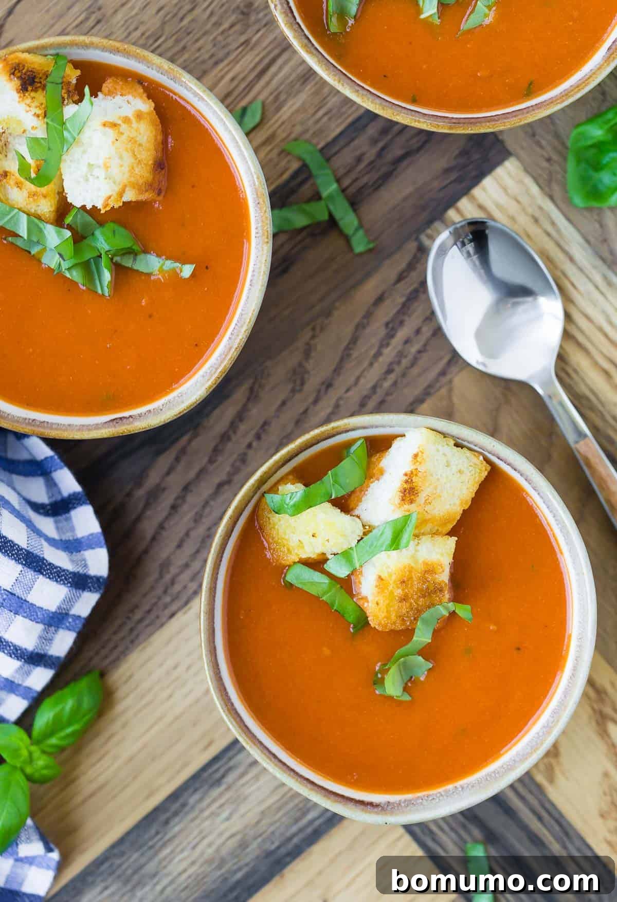 Overhead view of three small bowls of instant pot tomato soup, topped with croutons and fresh basil.