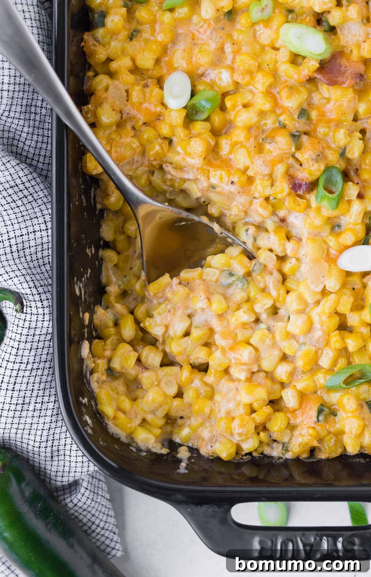 Overhead view of corn casserole in a black baking dish, sprinkled with green onions.