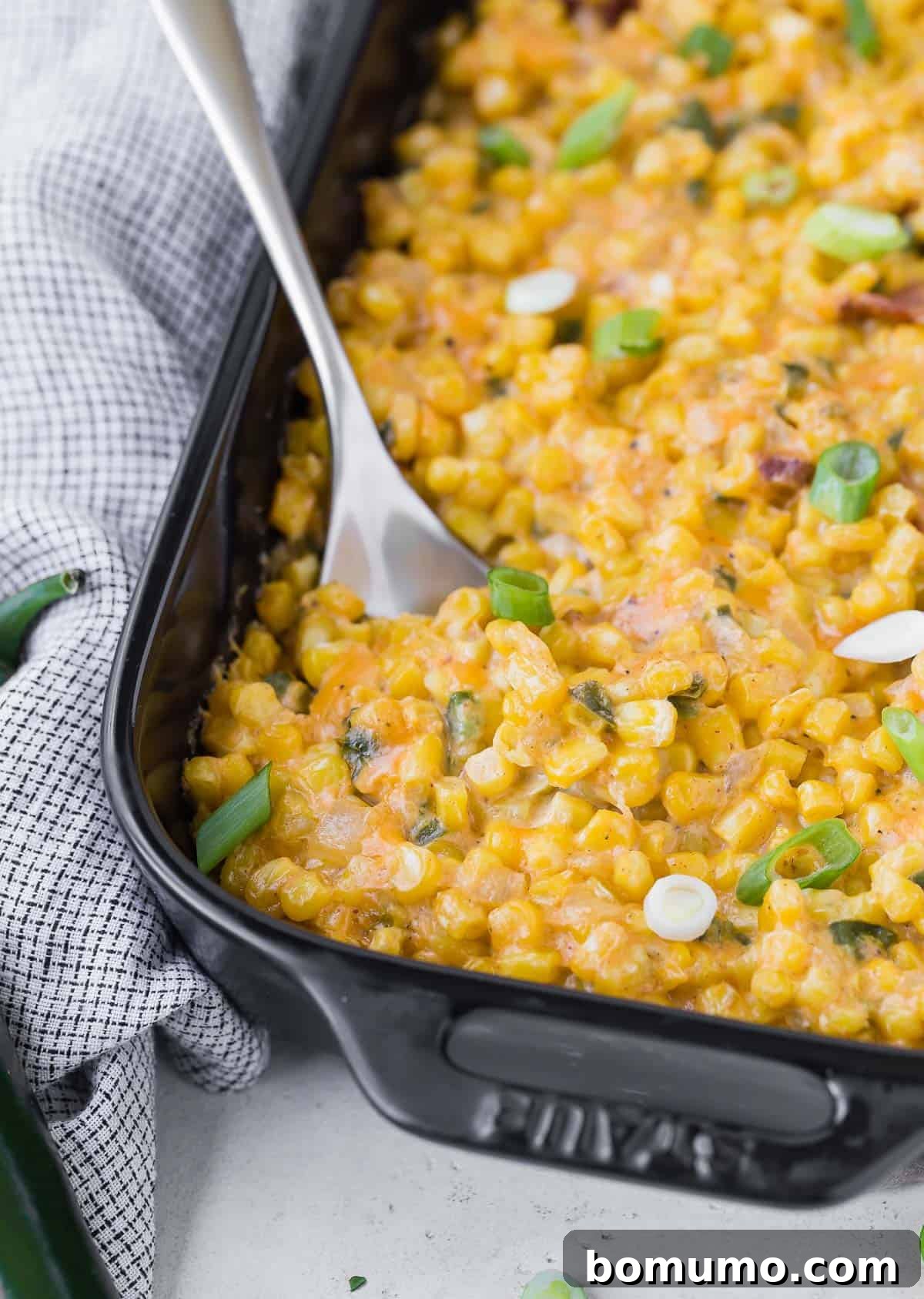 Corn and cheese casserole being scooped out of a black baking dish.
