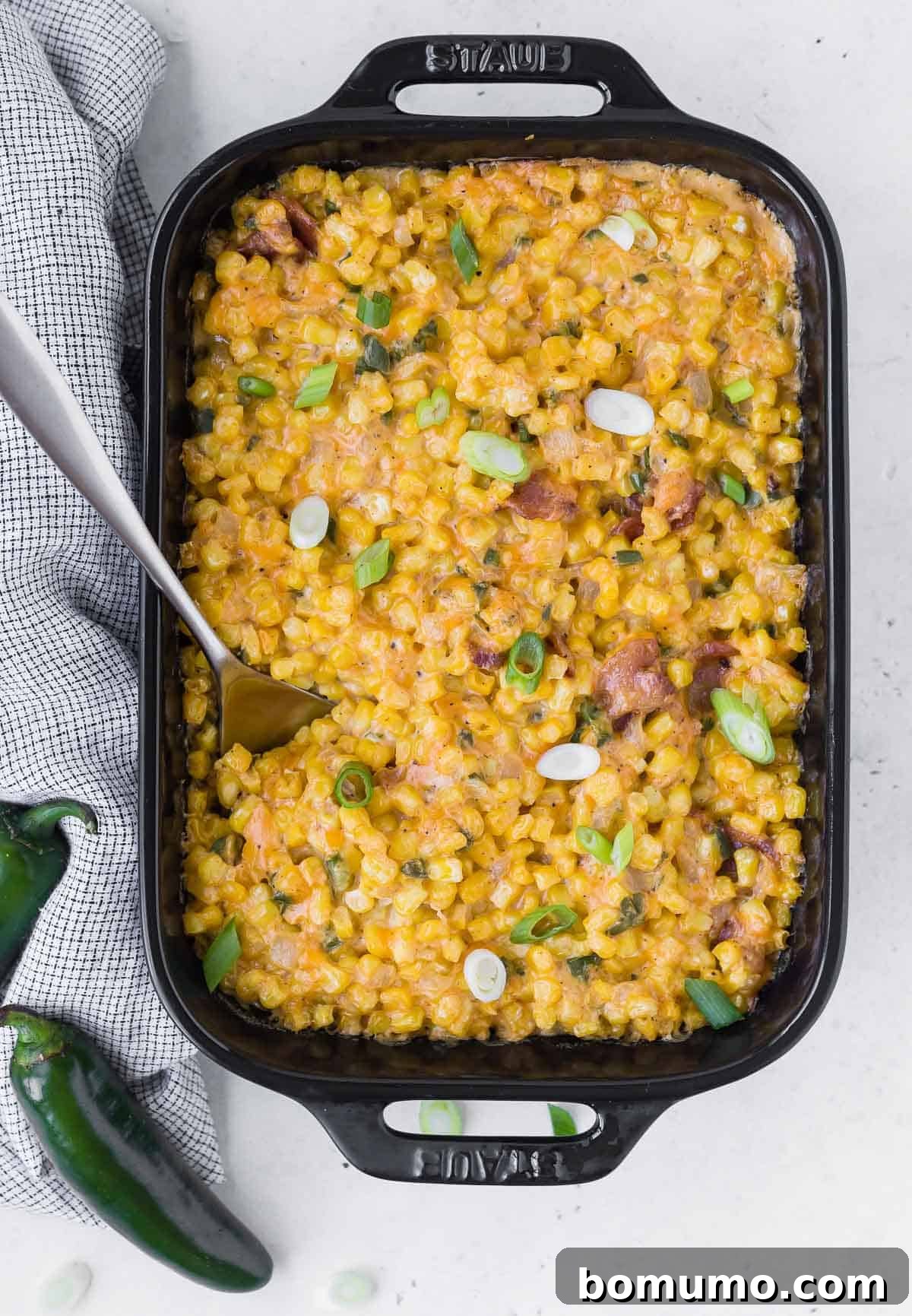 Full overhead view of a black casserole dish filled with cheese, corn, jalapeno, and bacon.