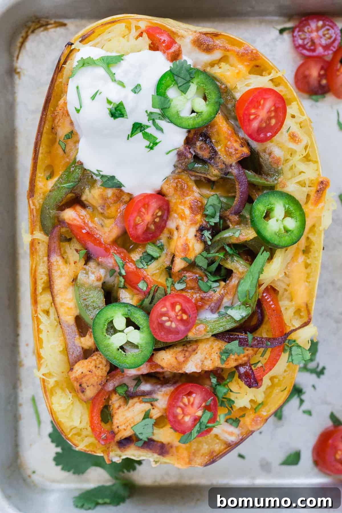 Overhead view of a spaghetti squash half, generously stuffed with seasoned chicken, vibrant bell peppers, and savory onions, all topped with melted cheese and fresh fajita garnishes. A perfect healthy, low-carb meal.