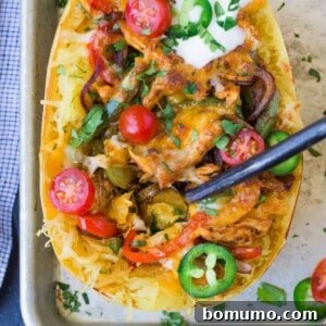 Spaghetti squash filled with colorful bell peppers, onions, seasoned chicken, and melted cheese, finished with fresh toppings like sour cream, jalapeño, and tomato for a complete, healthy meal.