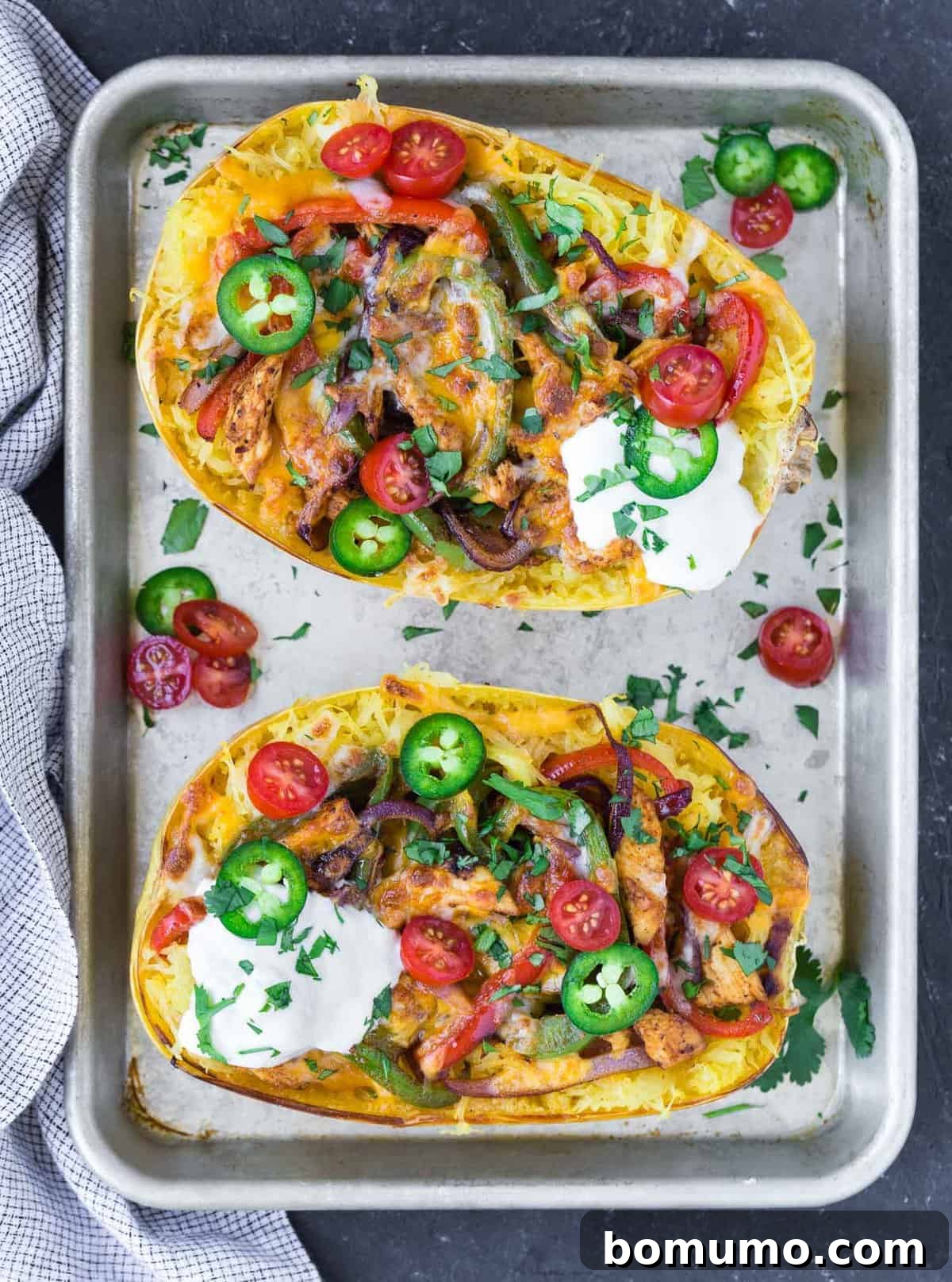 Two halves of perfectly roasted spaghetti squash, piled high with colorful chicken fajita filling, including seasoned chicken, bell peppers, and onions, topped with a generous layer of cheese.