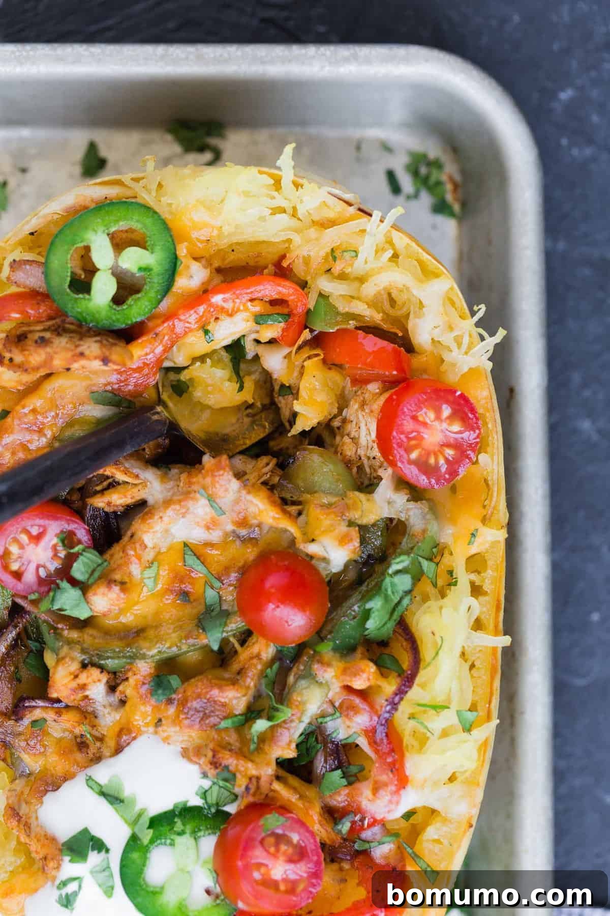 A close-up shot of a richly garnished chicken fajita stuffed spaghetti squash, adorned with fresh sour cream, diced tomatoes, and sliced jalapeños, ready for serving.