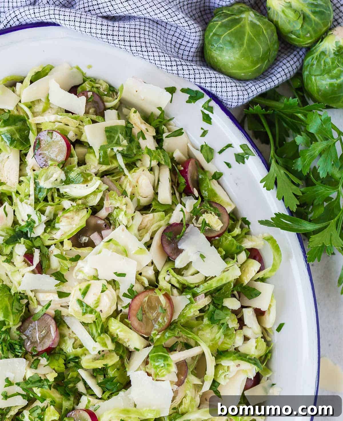 A close-up view of the shaved Brussels sprouts salad, highlighting the delicate textures of the sprouts, the vibrant grapes, and the savory Parmesan cheese.