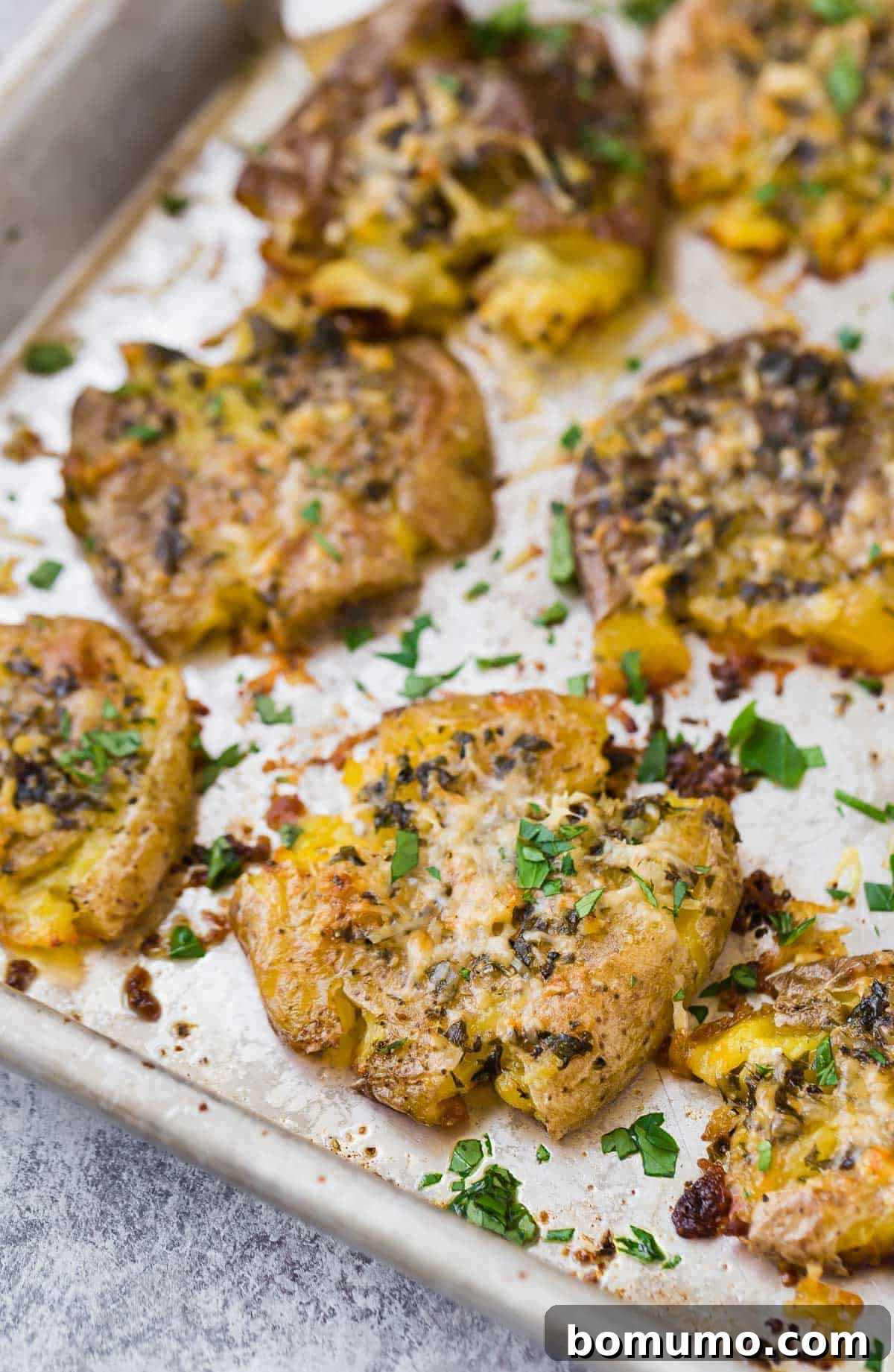 Close up of a crispy smashed potato on a sheet pan with others.