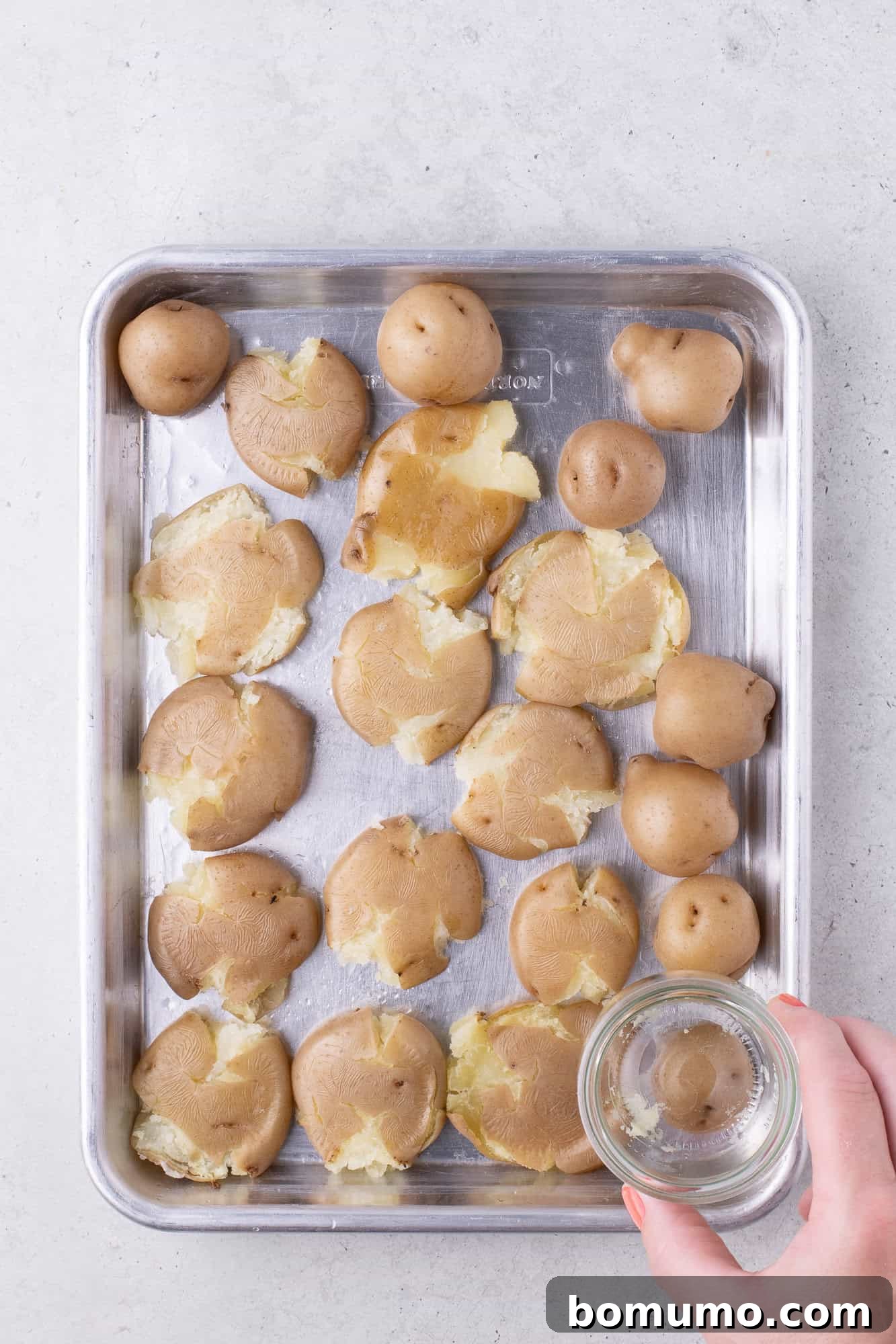 Baby potatoes on a sheet pan, being smashed with a small glass.