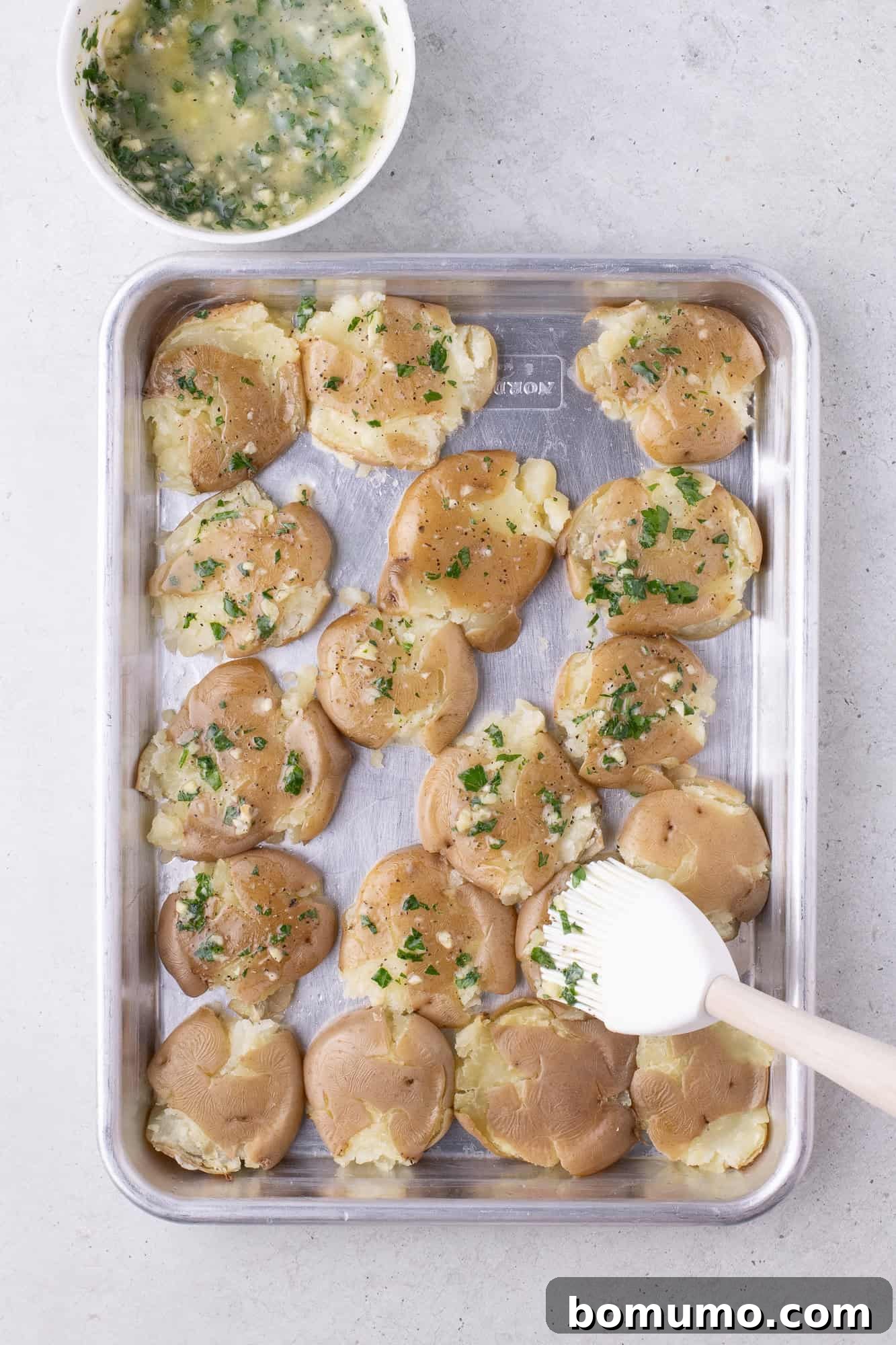Garlic butter being brushed on smashed potatoes.