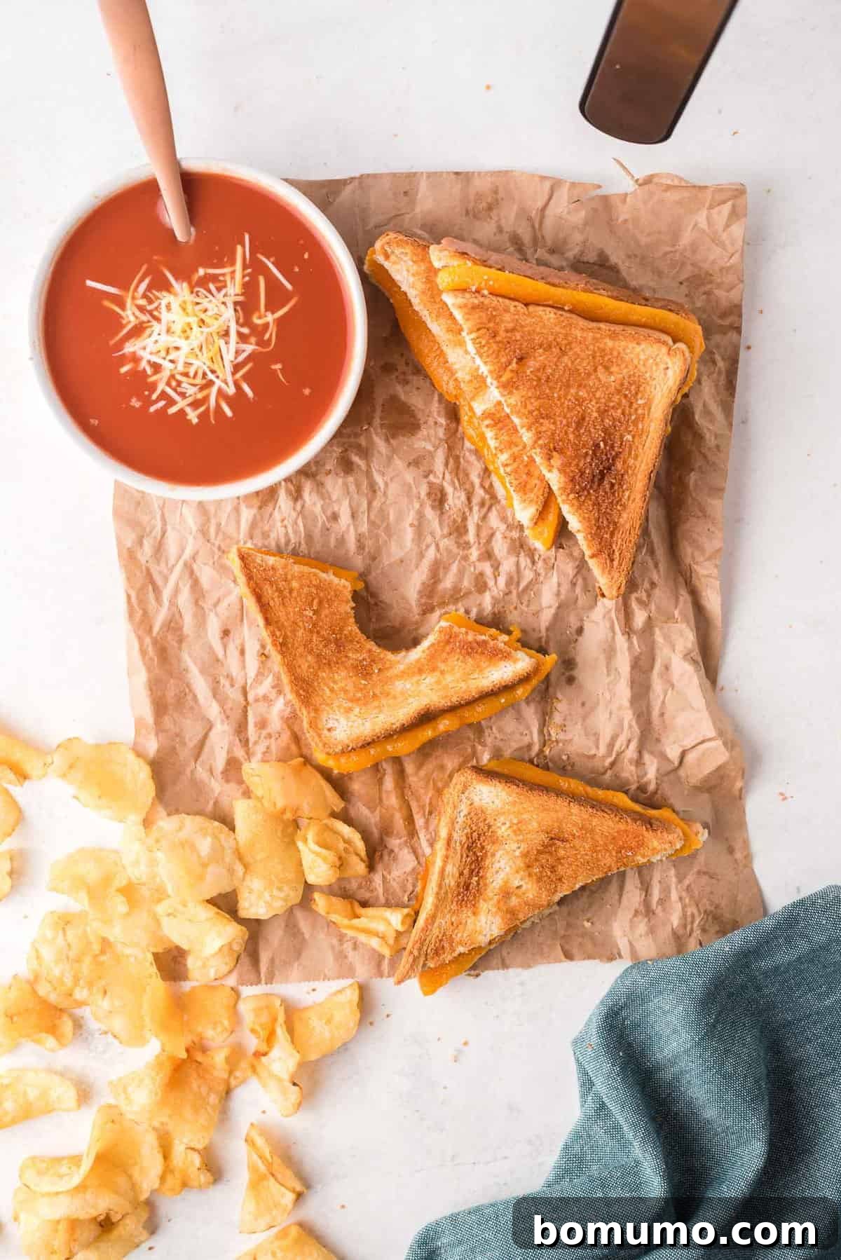 Toasted sandwich with cheese, alongside potato chips and tomato soup.