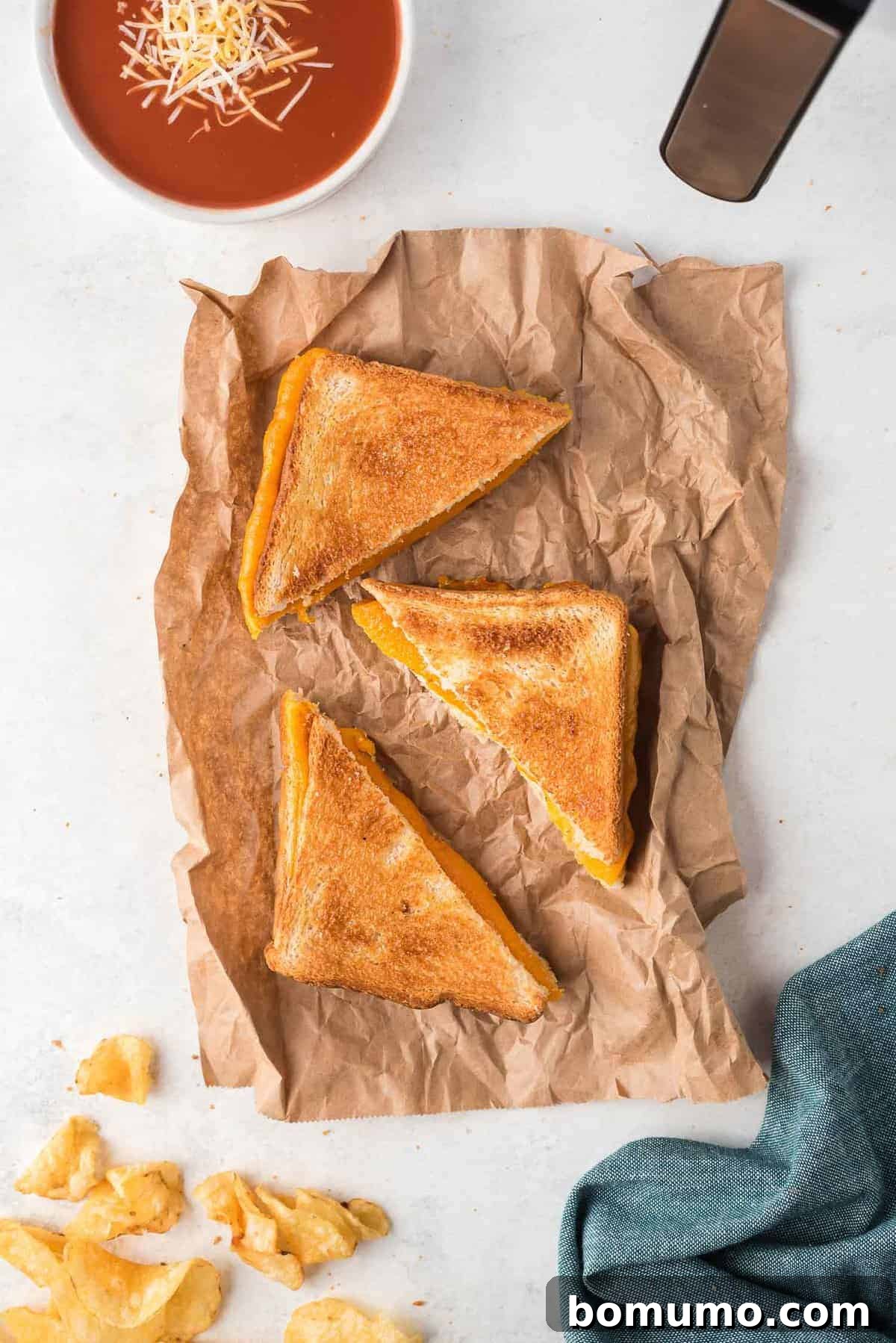 Overhead view of toasted sandwich halves, potato chips, and a bowl of cheese topped tomato soup.