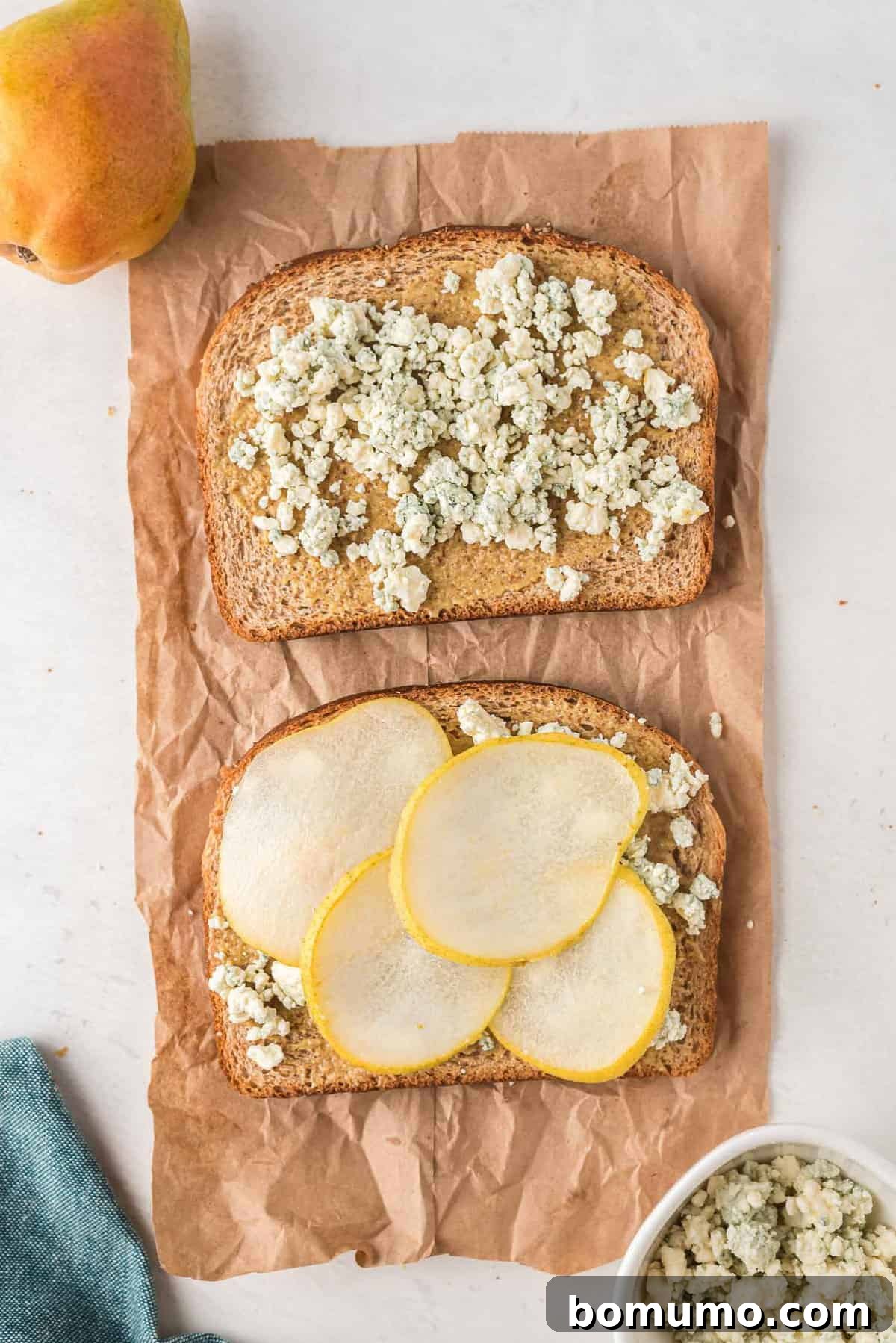 An open faced grilled cheese before it is cooked, containing pears and blue cheese crumbles.