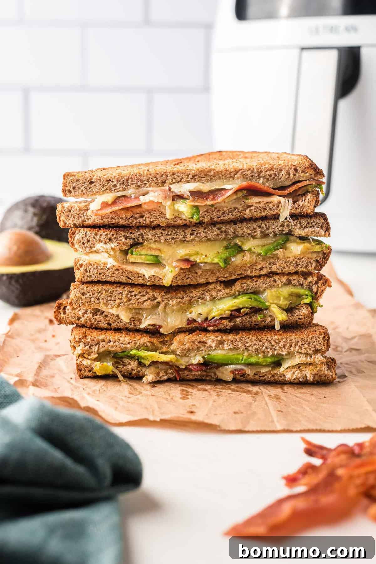 Stacked sandwich halves filled with bacon, avocado, and melted cheese. 