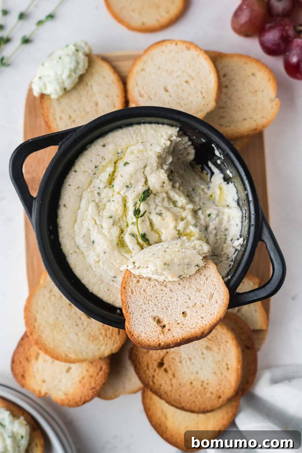 Bread being dipped into goat cheese dip in a black pan.