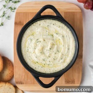 Overhead view of a small black pan with goat cheese dip, sprinkled with fresh thyme.