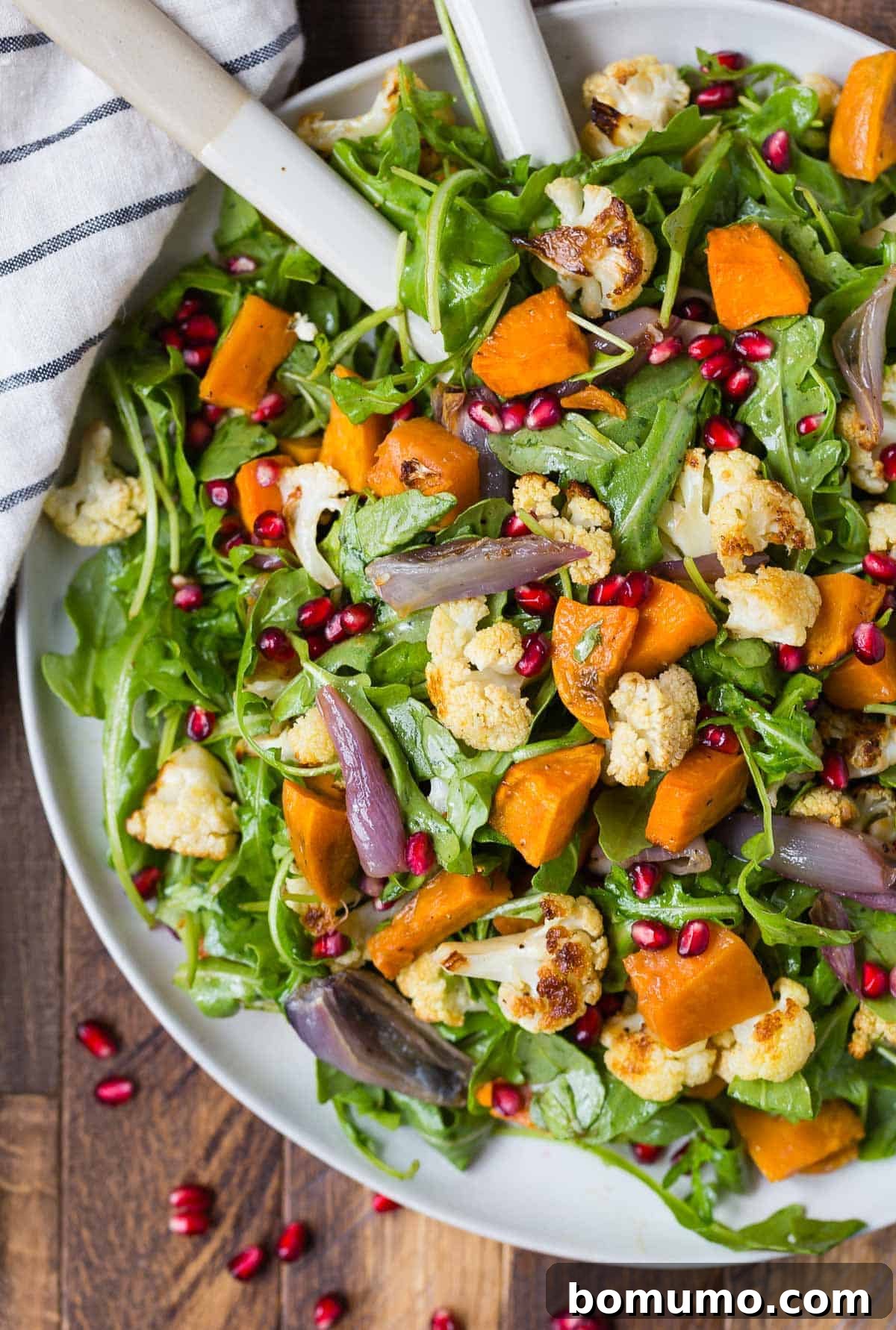 A vibrant, healthy salad featuring roasted cauliflower, sweet potatoes, fresh arugula, and juicy pomegranate seeds, drizzled with a rich vinaigrette.
