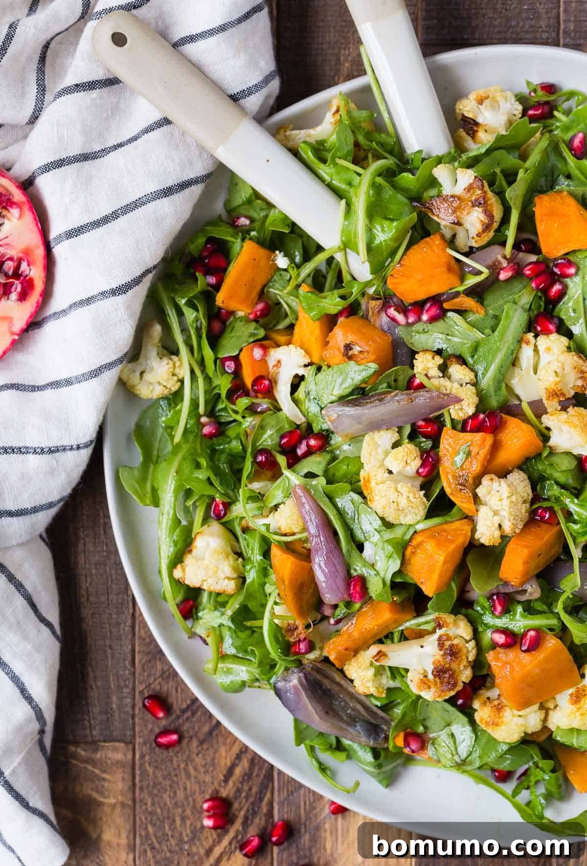 A close-up shot of a beautiful fall salad, showcasing roasted cauliflower, sweet potatoes, and vibrant pomegranate arils, ready to be served.