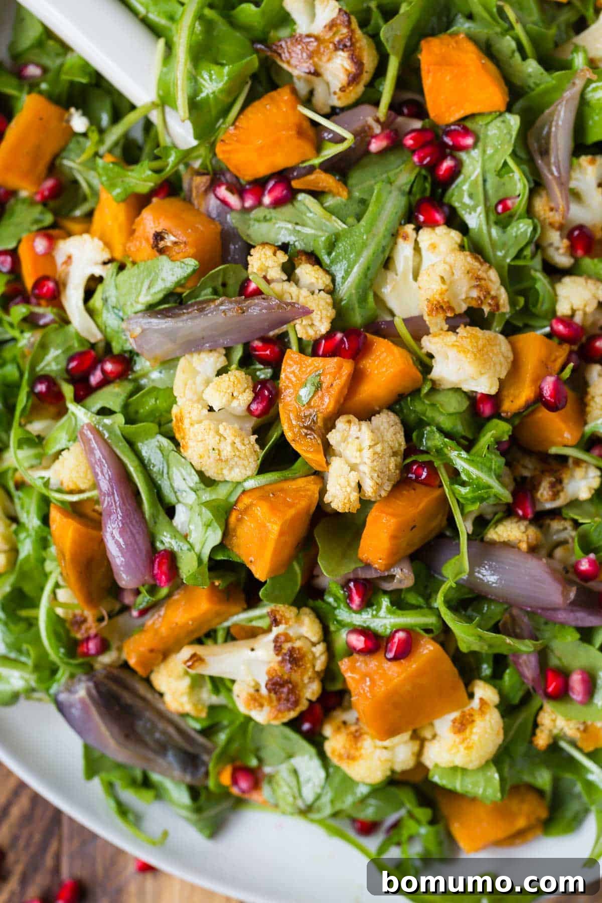 A close-up view of a fresh arugula salad, generously topped with perfectly roasted cauliflower and tender sweet potatoes, highlighted by the vibrant green leaves.