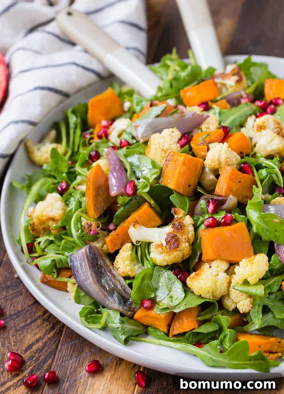 A beautifully composed salad with roasted cauliflower, glistening pomegranate arils, and tender sweet potatoes, served on a white platter.