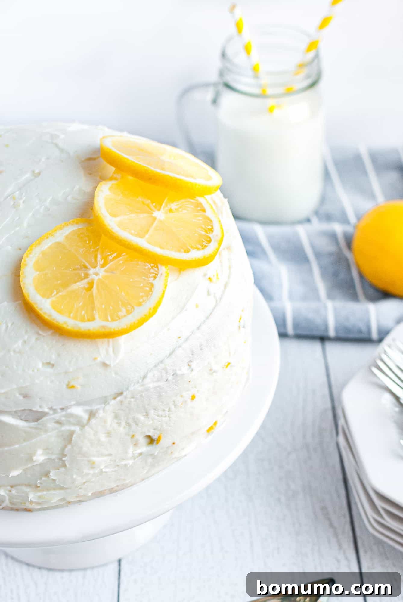 A beautifully garnished lemon cake, featuring fresh lemon slices and zest atop a pristine white frosting.