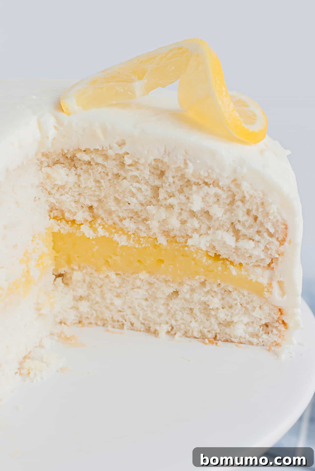 A beautifully presented white cake with lemon filling and a thick layer of lemon cream cheese frosting, ready to be served.