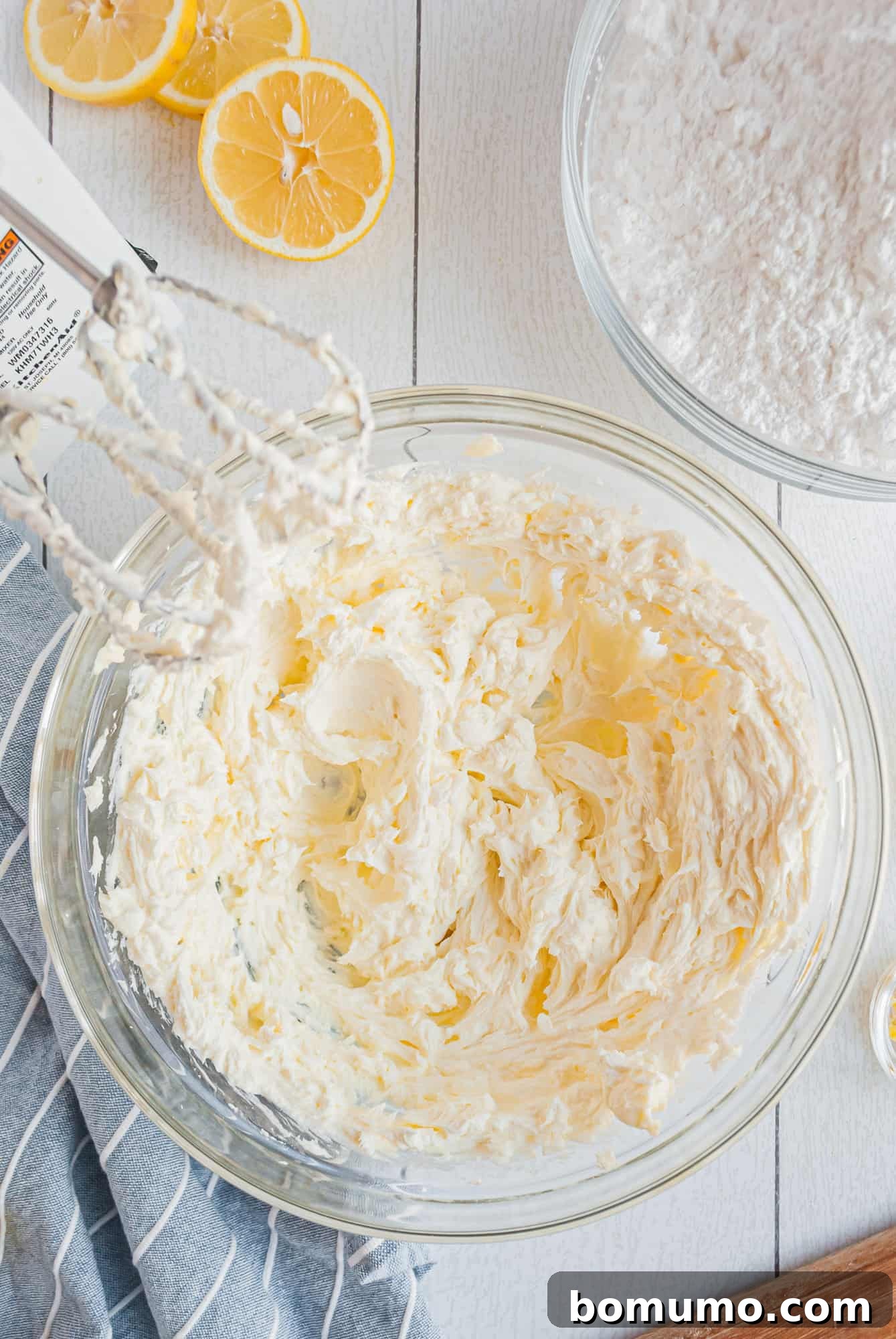 A mixing bowl filled with creamy, light yellow lemon cream cheese frosting, ready for spreading.