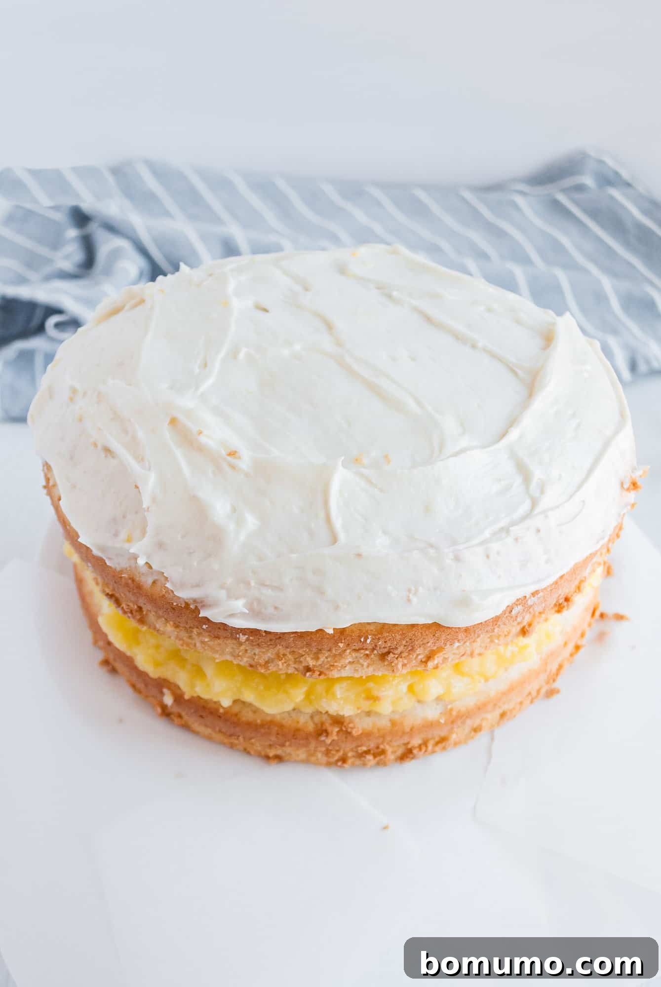 Two cake layers being assembled, with lemon filling spread between them, ready for the top layer.
