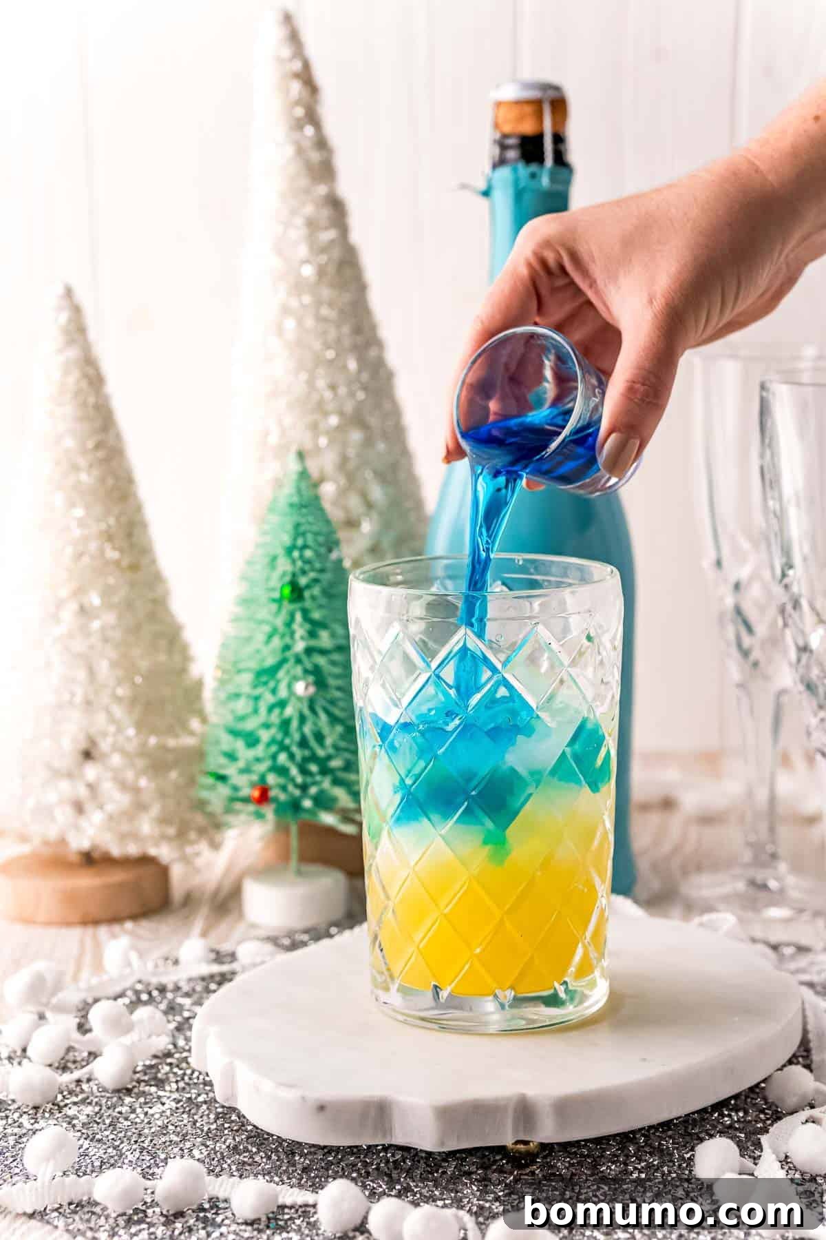 Blue liquid being poured into pineapple juice, creating a mesmerizing blend for the Jack Frost Mimosa.