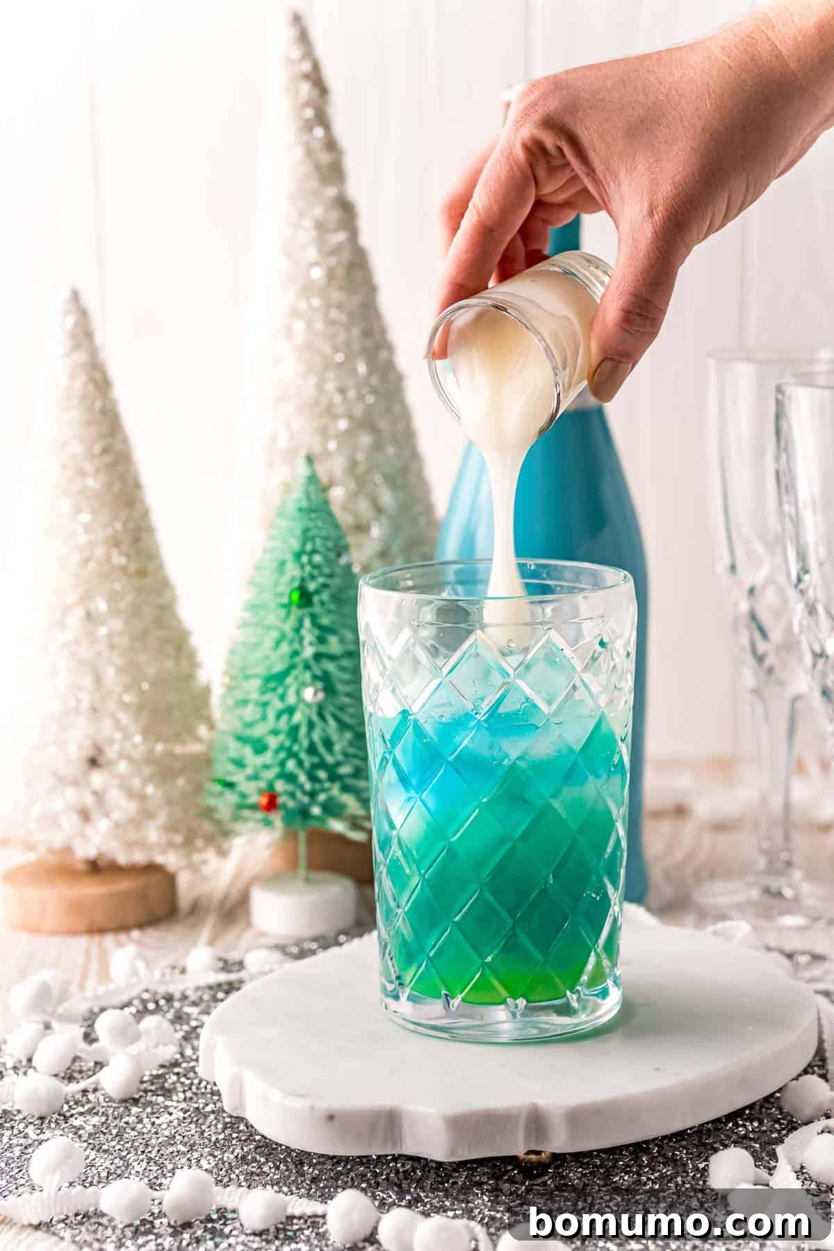 White liquid being poured into blue liquid, illustrating the creamy coconut component of the cocktail.