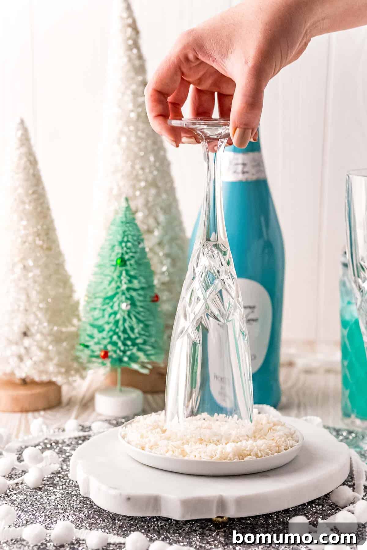 Champagne flute being rimmed with simple syrup and coconut flakes, creating a festive, frosty edge.