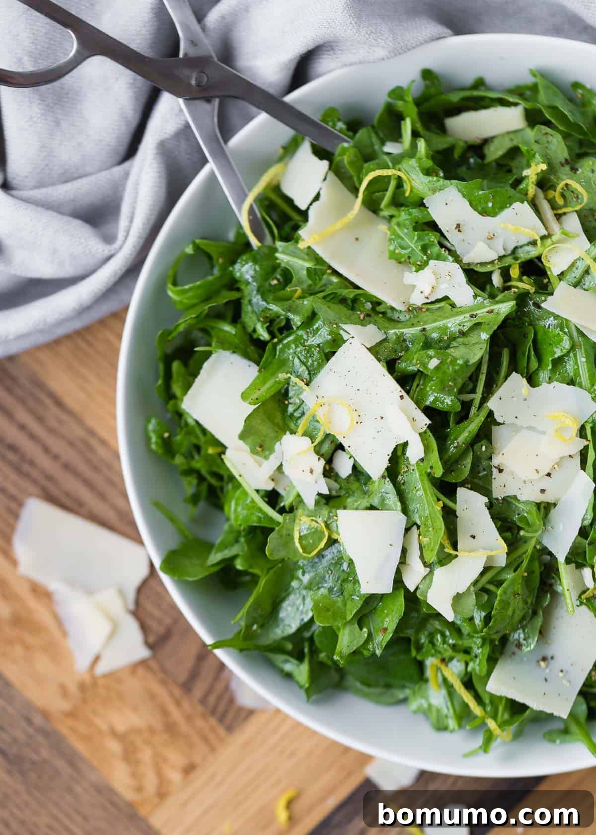 Overhead view of a classic arugula salad with shaved Parmesan and lemon slices, dressed in a light vinaigrette.