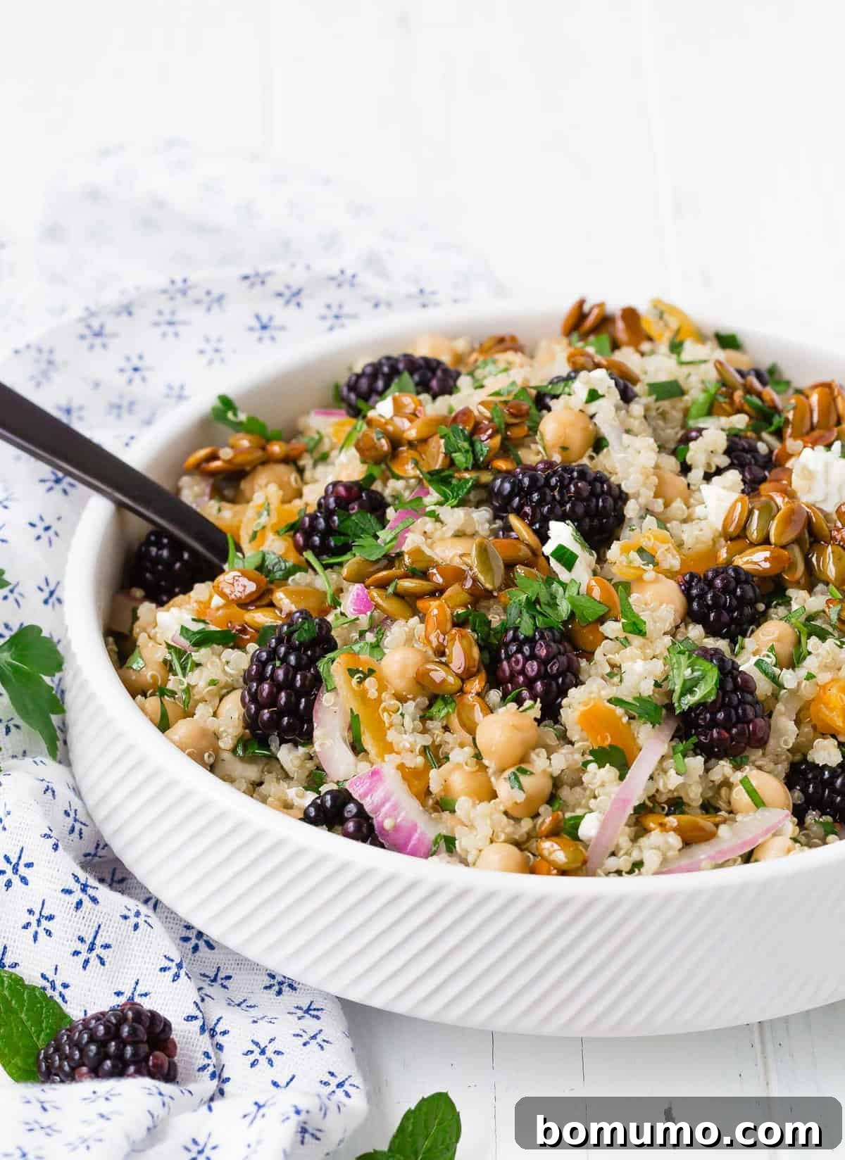 Colorful quinoa salad in a white bowl with a black spoon.