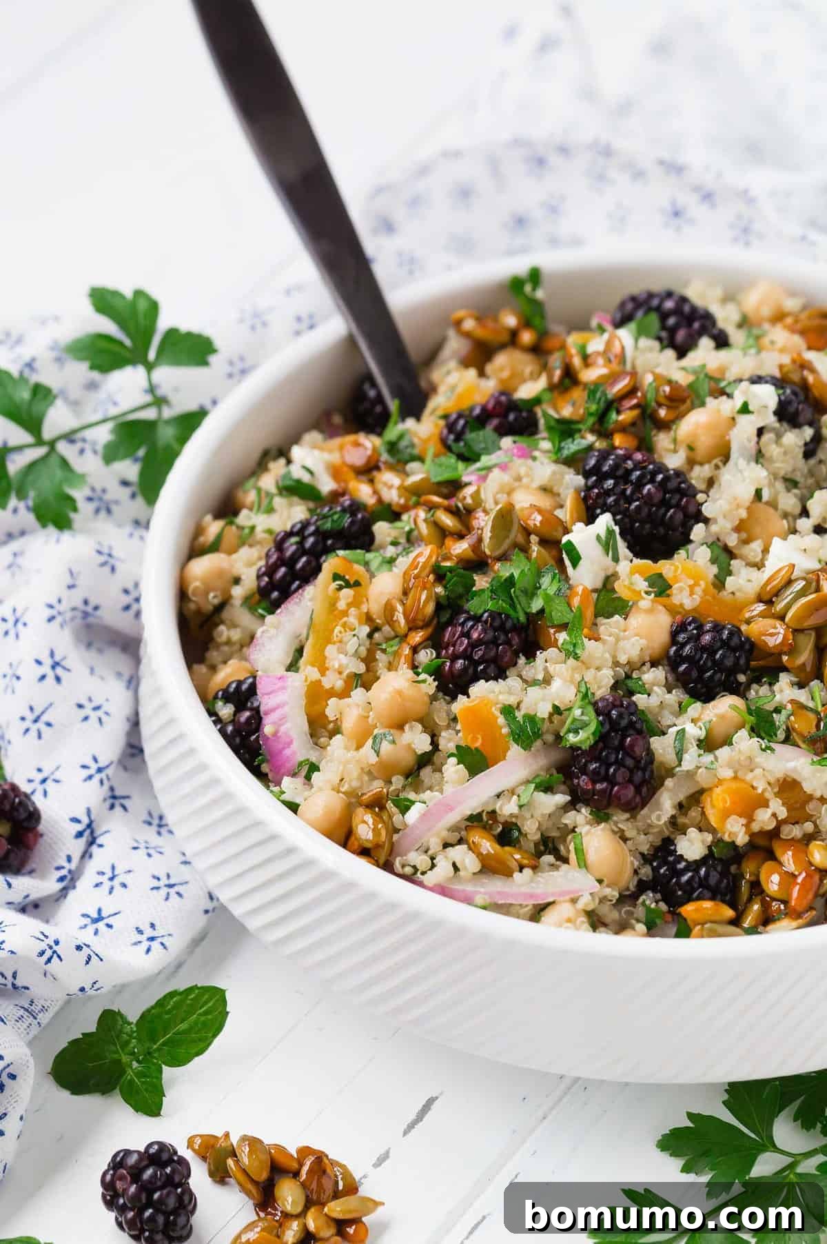 Hearty quinoa salad in a white bowl with a black spoon.