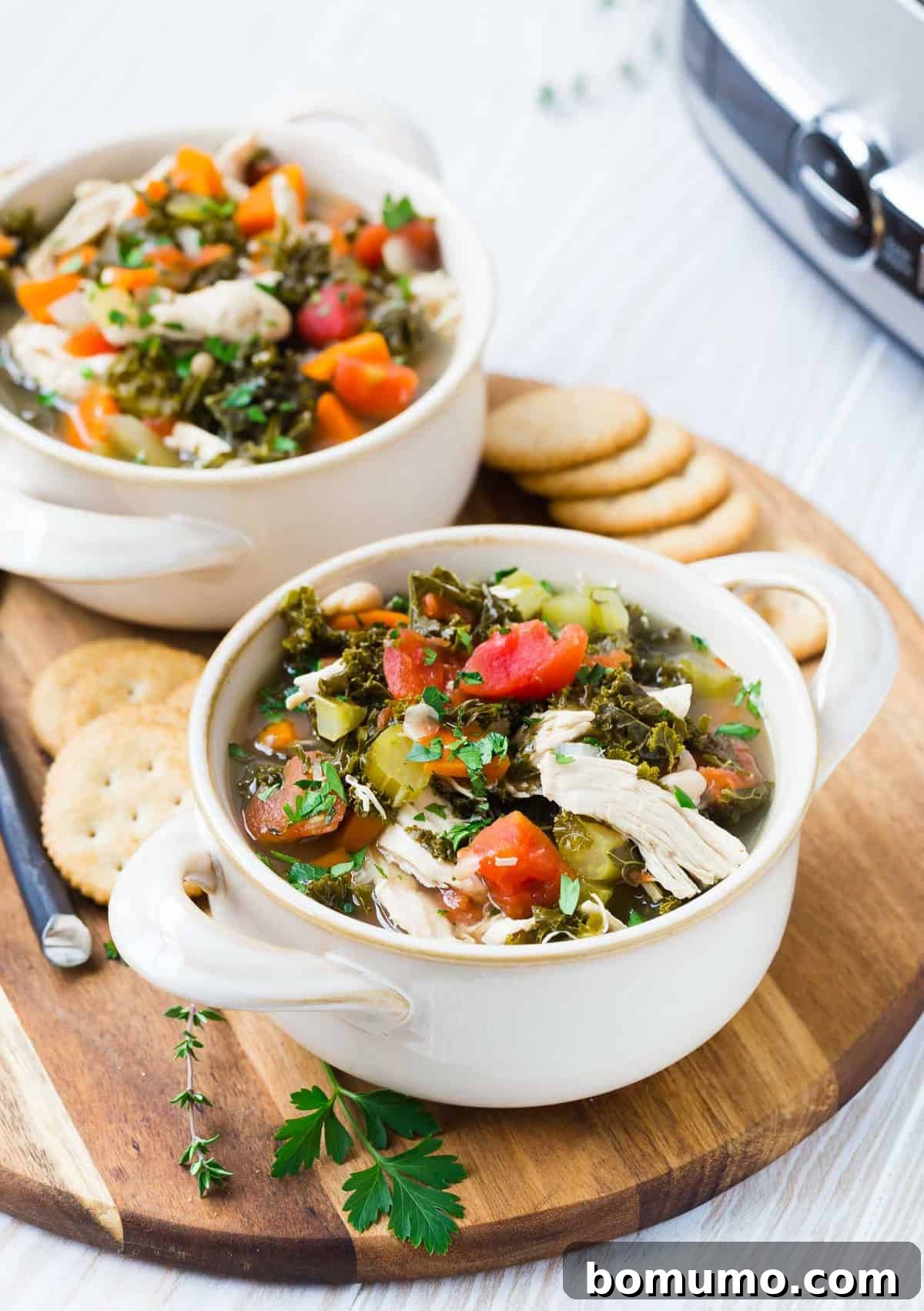 Two white bowls full of chicken and kale soup, garnished with fresh parsley.