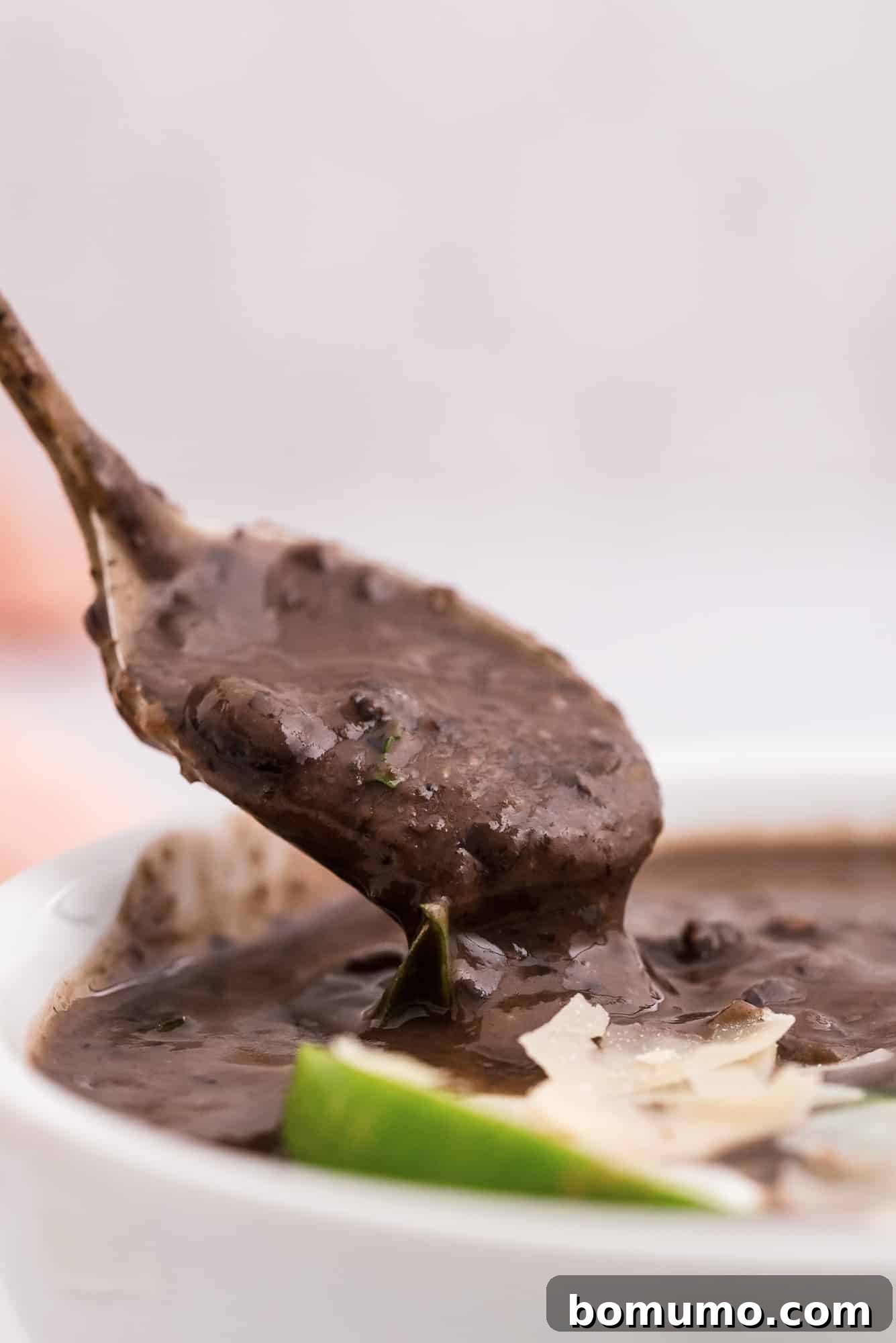 A spoon laden with creamy black bean soup being carefully lifted from a serving bowl, showcasing its rich texture.