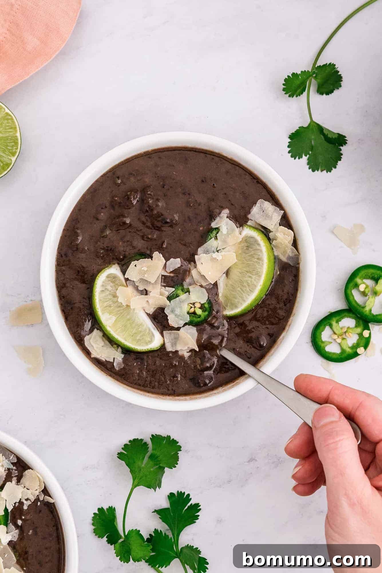 A hand gently holding a spoon, scooping rich black bean soup from a white bowl.