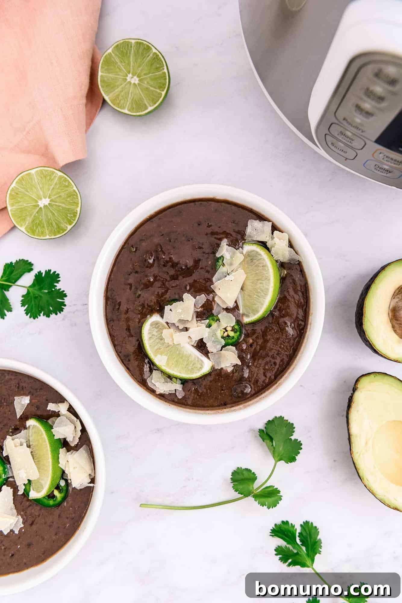 Two bowls of dark brown black bean soup, artfully garnished with fresh herbs and a swirl of cream, set against a rustic backdrop.