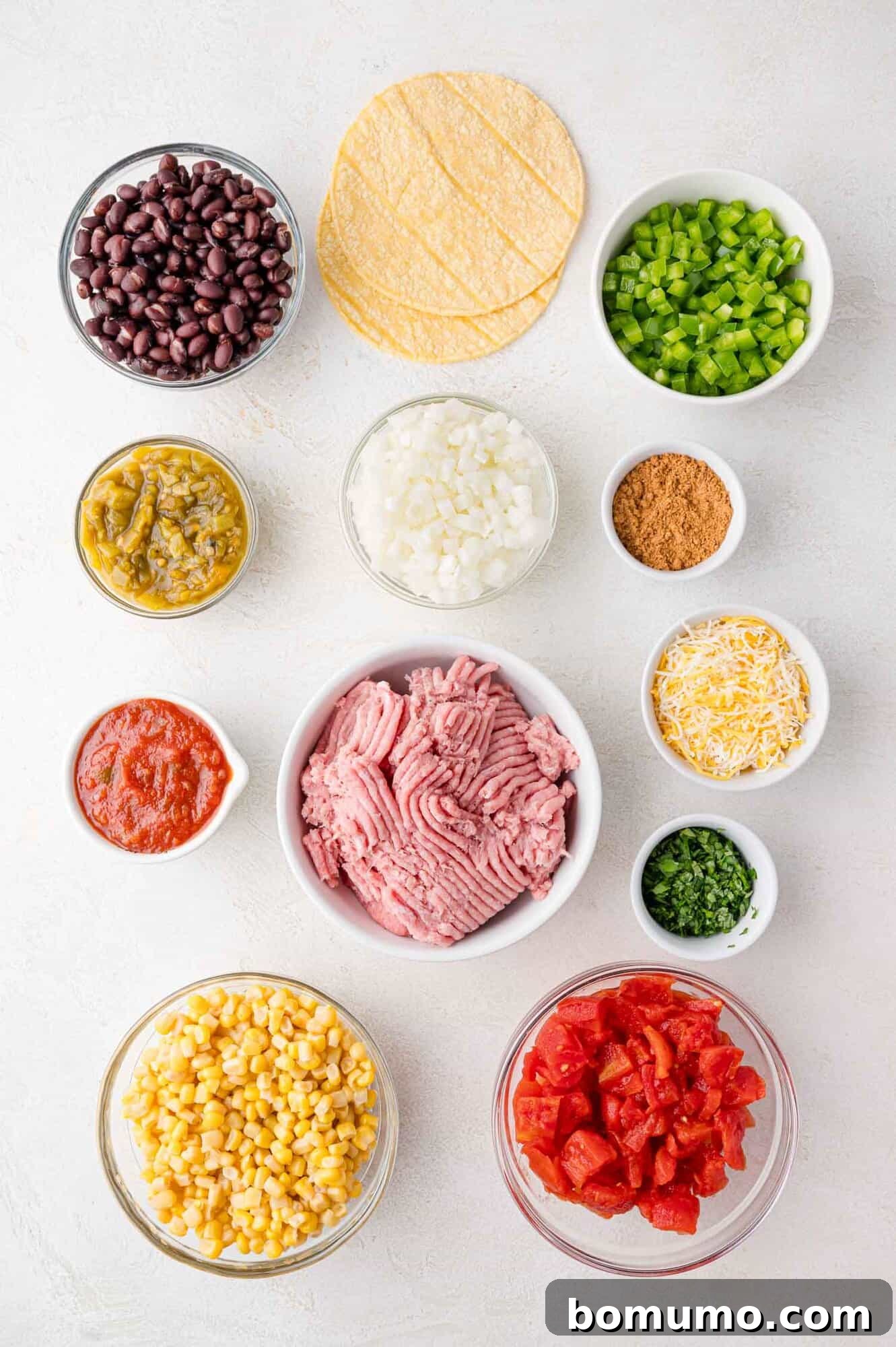 An inviting overhead shot of assorted fresh ingredients meticulously arranged on a clean white surface, showcasing the vibrant colors of ground meat, black beans, corn, diced tomatoes, onions, green chilies, shredded cheese, rich salsa, crisp bell pepper, savory seasoning, fragrant herbs, and golden corn tortillas.