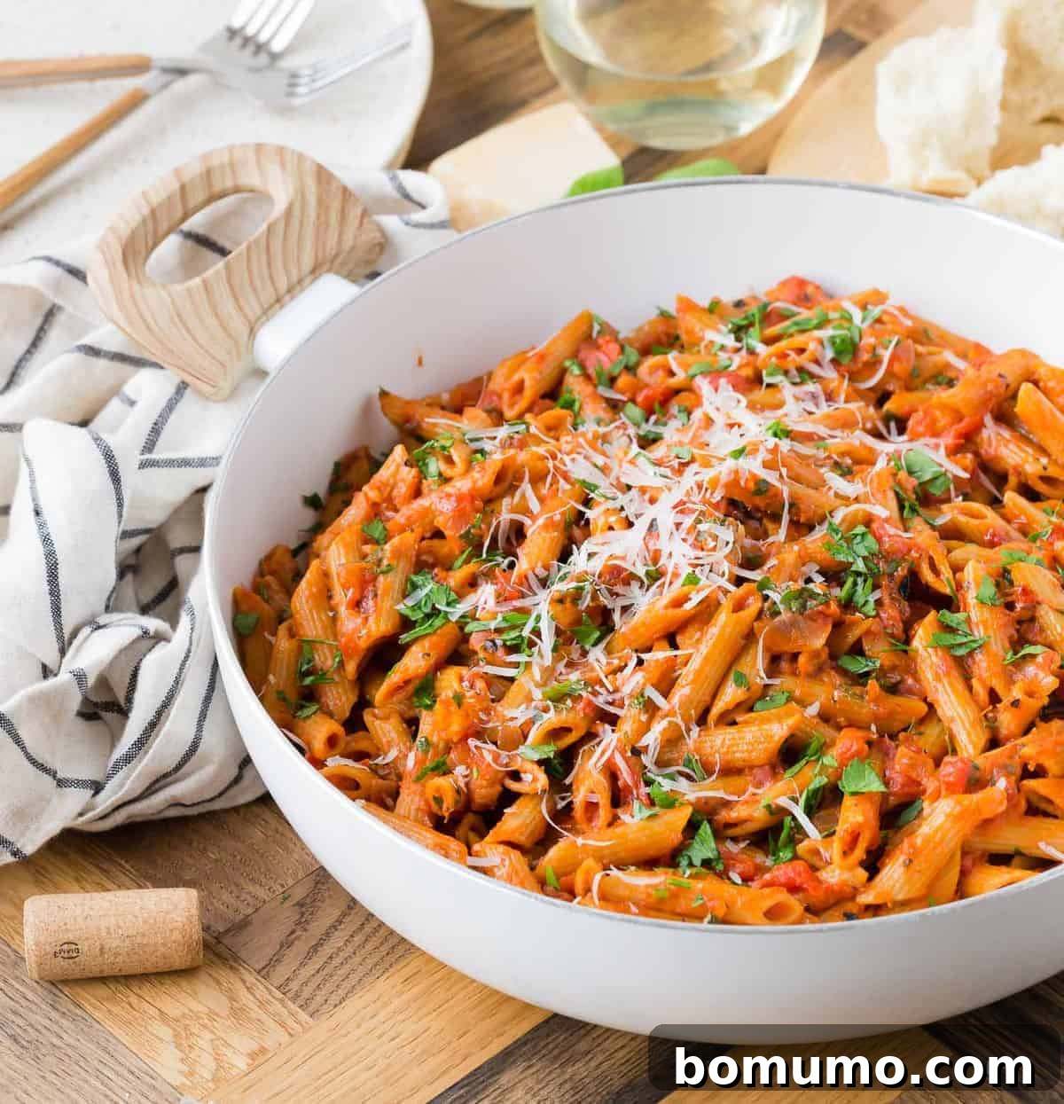Pasta in a white, wooden handled pan, with wine in background.