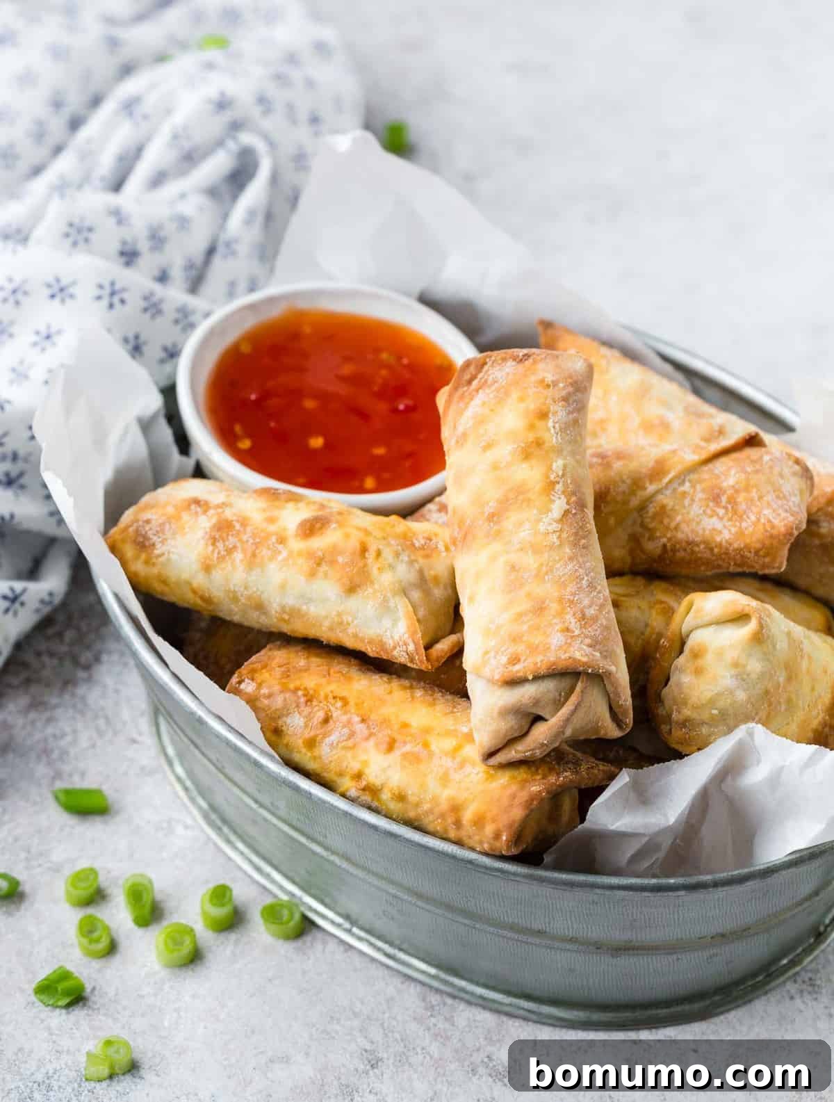 Crispy air fryer egg rolls arranged in a metal basket, accompanied by a small bowl of vibrant dipping sauce.