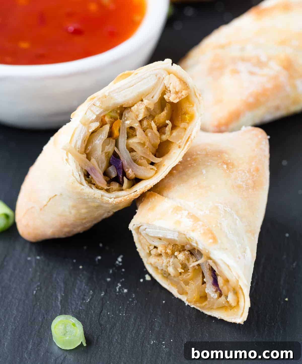 A perfectly cut air fried egg roll revealing its vibrant, savory filling on a dark surface.