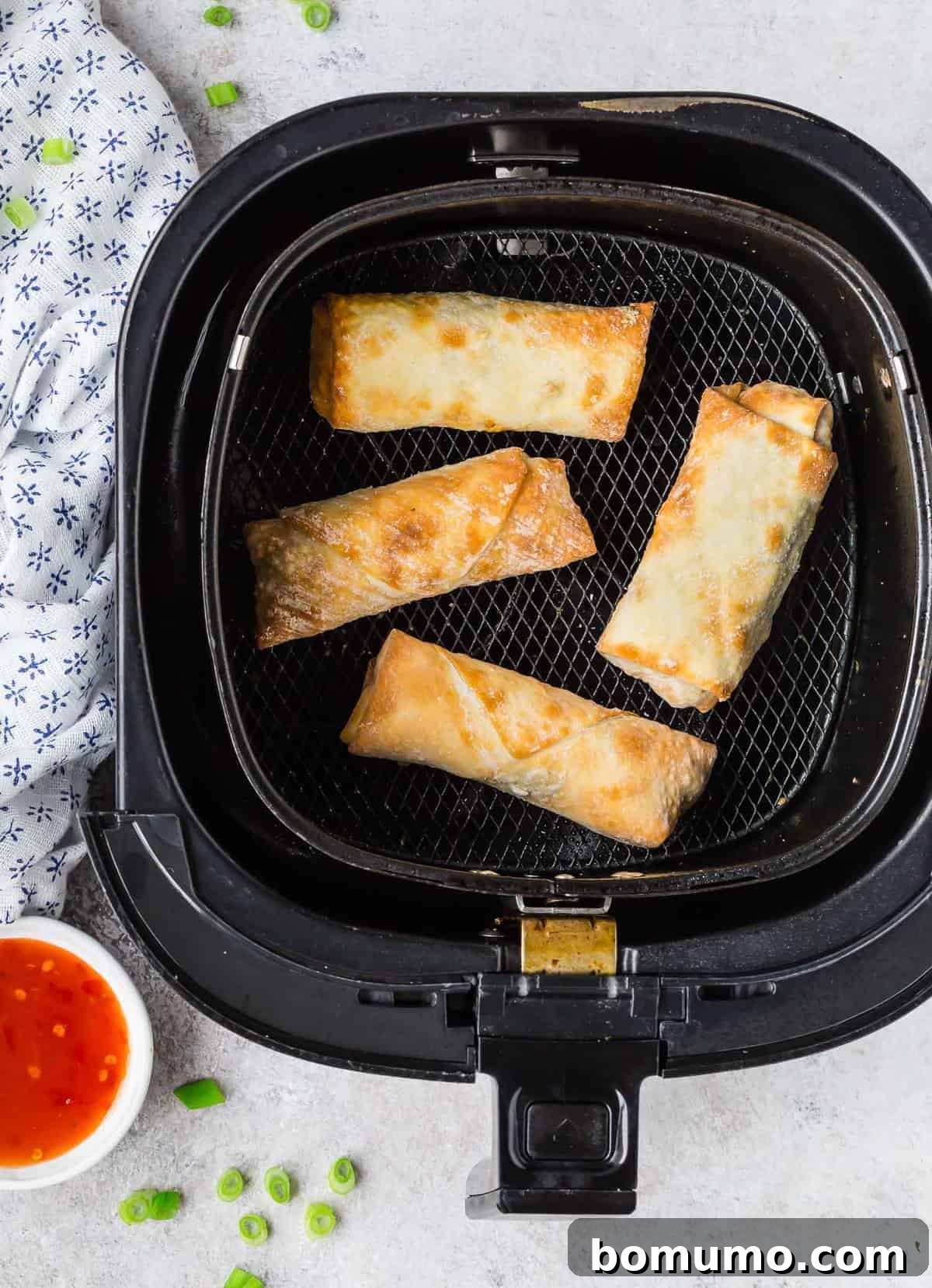 Overhead view of several golden brown egg rolls arranged neatly in an air fryer basket.