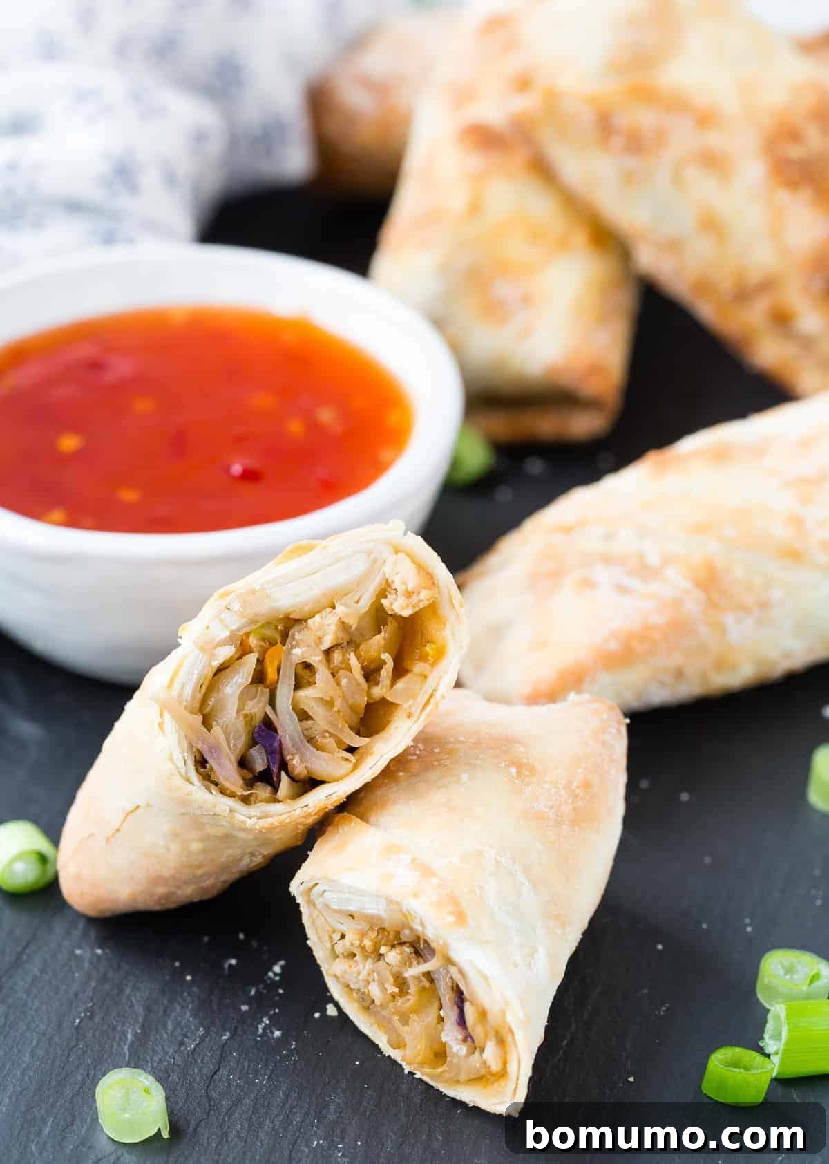 An air fried egg roll, perfectly cut in half to reveal its rich, vibrant filling, resting on a dark slate surface.